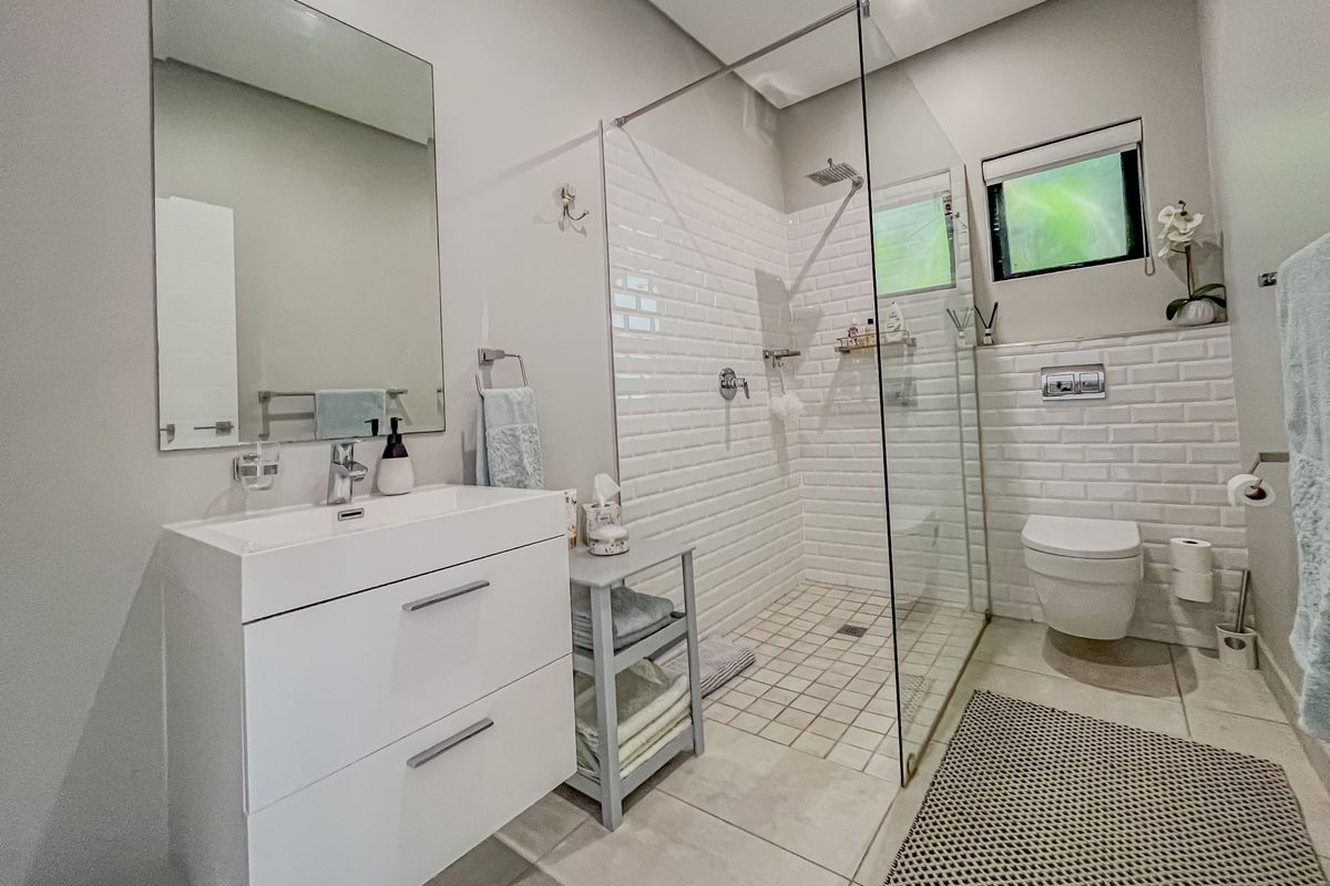 Modern bathroom featuring a frameless glass walk-in shower, subway tile backsplash, wall-mounted toilet, and a contemporary vanity with a large mirror.
