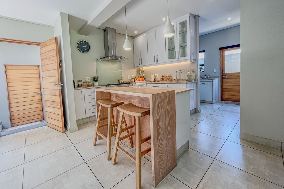 Modern kitchen featuring white cabinetry, stone countertops, stainless steel extractor fan, and a central breakfast island with integrated seating, leading to a scullery area.