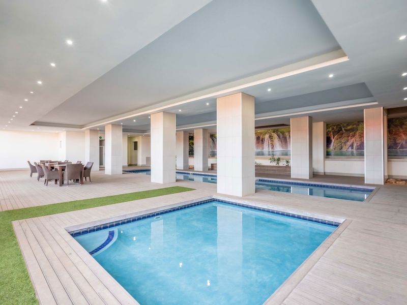 A spacious indoor pool area featuring multiple swimming pools, tiled decking, recessed ceiling lighting, and decorative wall murals.