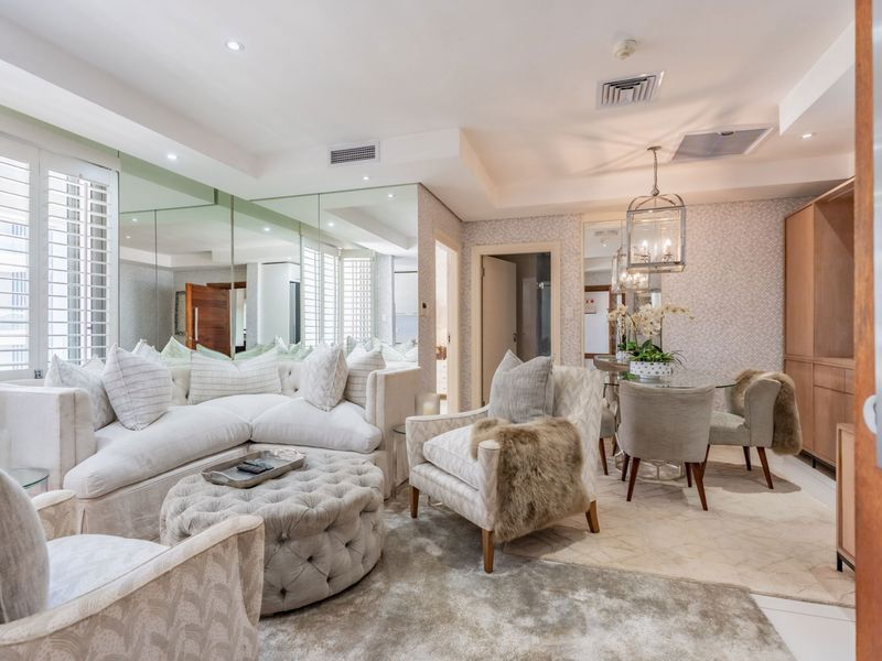 An elegant open-plan living and dining area featuring mirrored wall panels, recessed ceiling lighting, ducted air conditioning, and plantation shutters.