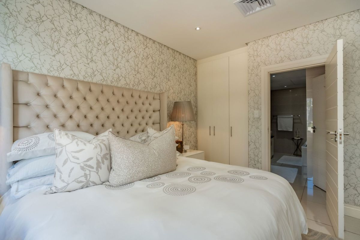 A well-appointed bedroom featuring built-in wardrobes, patterned wallpaper, and an en-suite bathroom with tiled finishes.