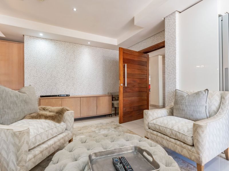 A well-maintained living area featuring recessed ceiling lighting, patterned wallpaper, and a solid timber door leading to an adjacent space.