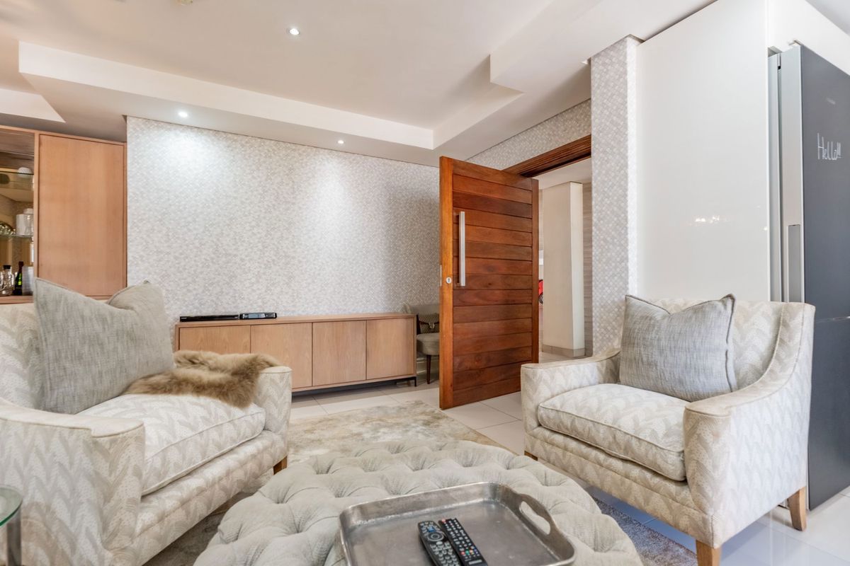 A well-maintained living area featuring recessed ceiling lighting, patterned wallpaper, and a solid timber door leading to an adjacent space.