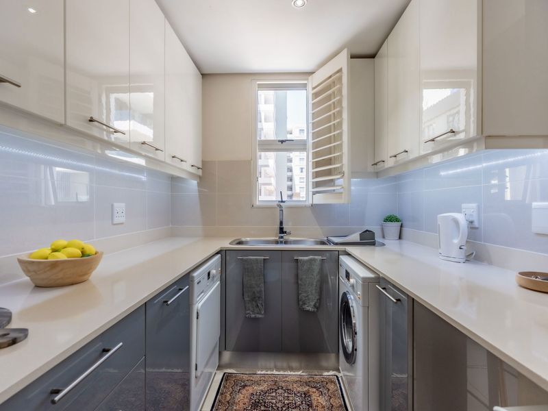 A modern, compact kitchen featuring high-gloss cabinetry, stone countertops, integrated sink, and built-in laundry appliances.