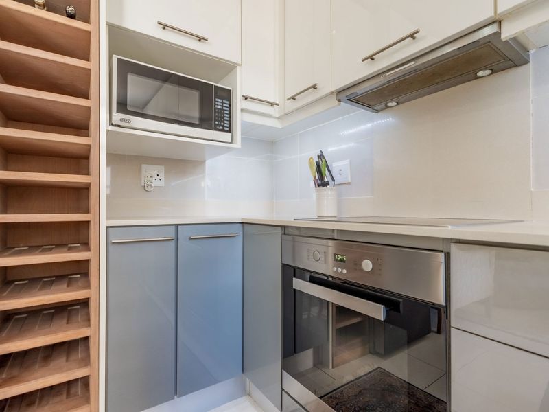 A compact, modern kitchen featuring built-in cabinetry, a stainless steel oven, electric cooktop, extractor fan, and a dedicated wine rack.