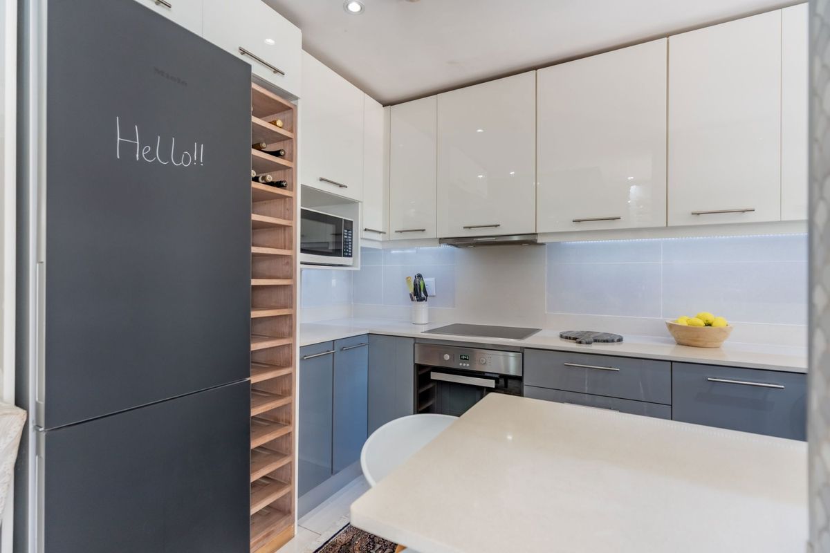 Modern kitchen featuring two-tone cabinetry, stone countertops, integrated oven, hob, extractor fan, and a built-in wine rack.