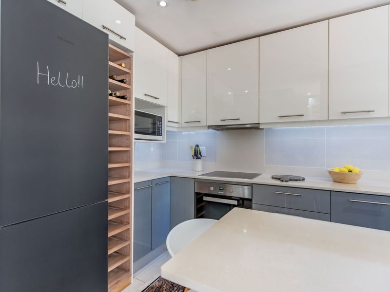 Modern kitchen featuring two-tone cabinetry, stone countertops, integrated oven, hob, extractor fan, and a built-in wine rack.