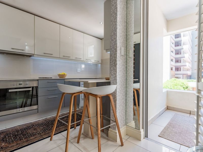 Modern kitchen featuring high-gloss cabinetry, integrated oven, and a breakfast bar, seamlessly connected to a bright balcony area.