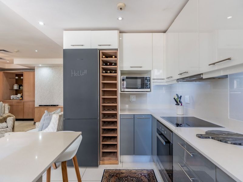 Modern open-plan kitchen featuring sleek white and grey cabinetry, integrated appliances, a built-in wine rack, and stone countertops, seamlessly flowing into the living area.