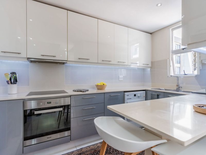Modern kitchen featuring high-gloss cabinetry, stone countertops, integrated oven, electric hob, extractor fan, and a breakfast bar area.