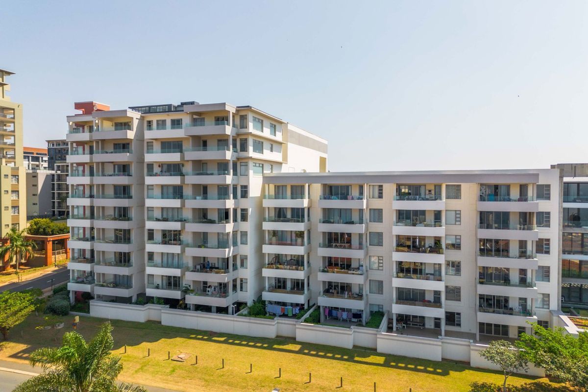 An aerial view of a modern multi-story apartment complex featuring private balconies and a landscaped ground-level garden area.
