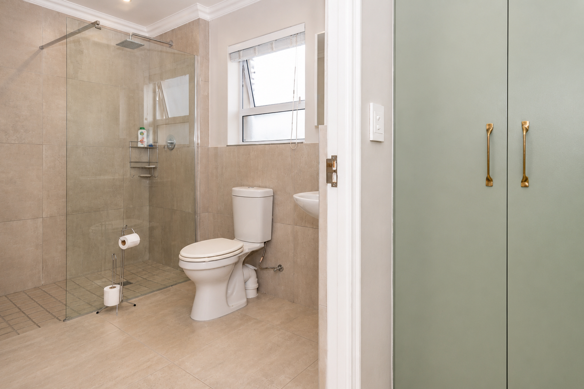 Modern bathroom featuring a walk-in glass shower, tiled walls, a white toilet, and a wall-mounted basin, adjacent to a sage green built-in cupboard.