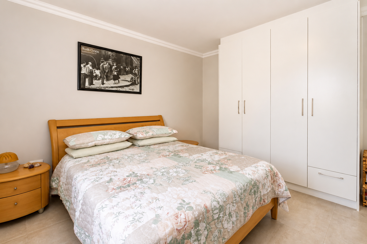 A well-maintained bedroom featuring neutral wall tones, tiled flooring, and ample storage provided by floor-to-ceiling built-in wardrobes.