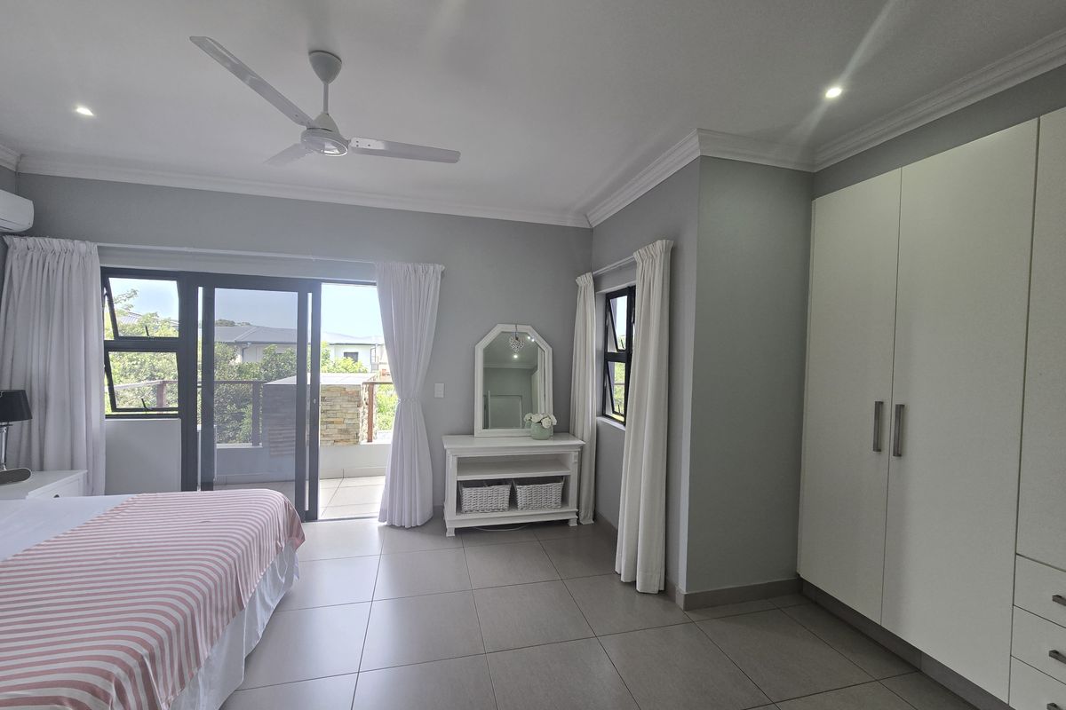 Spacious bedroom featuring large format floor tiles, built-in cupboards, a ceiling fan, and sliding glass doors opening onto a private balcony.