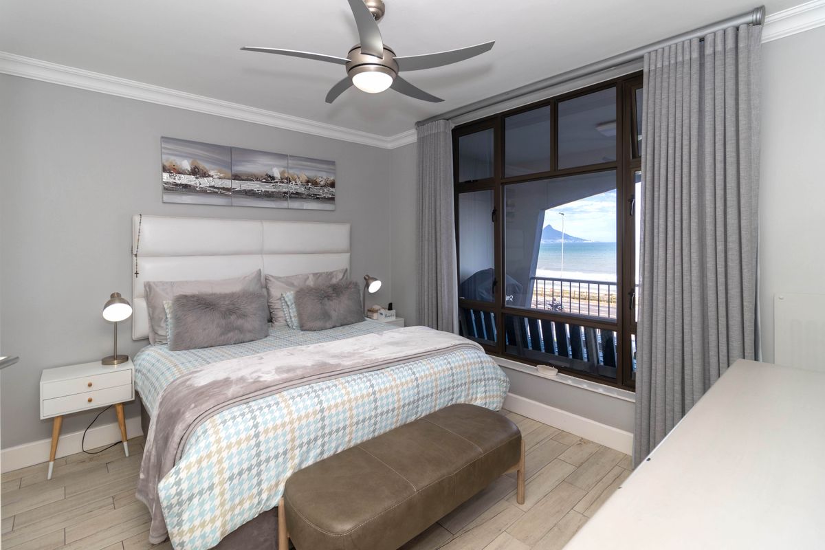 A well-maintained bedroom featuring tiled flooring, a modern ceiling fan, and large windows offering scenic coastal views.