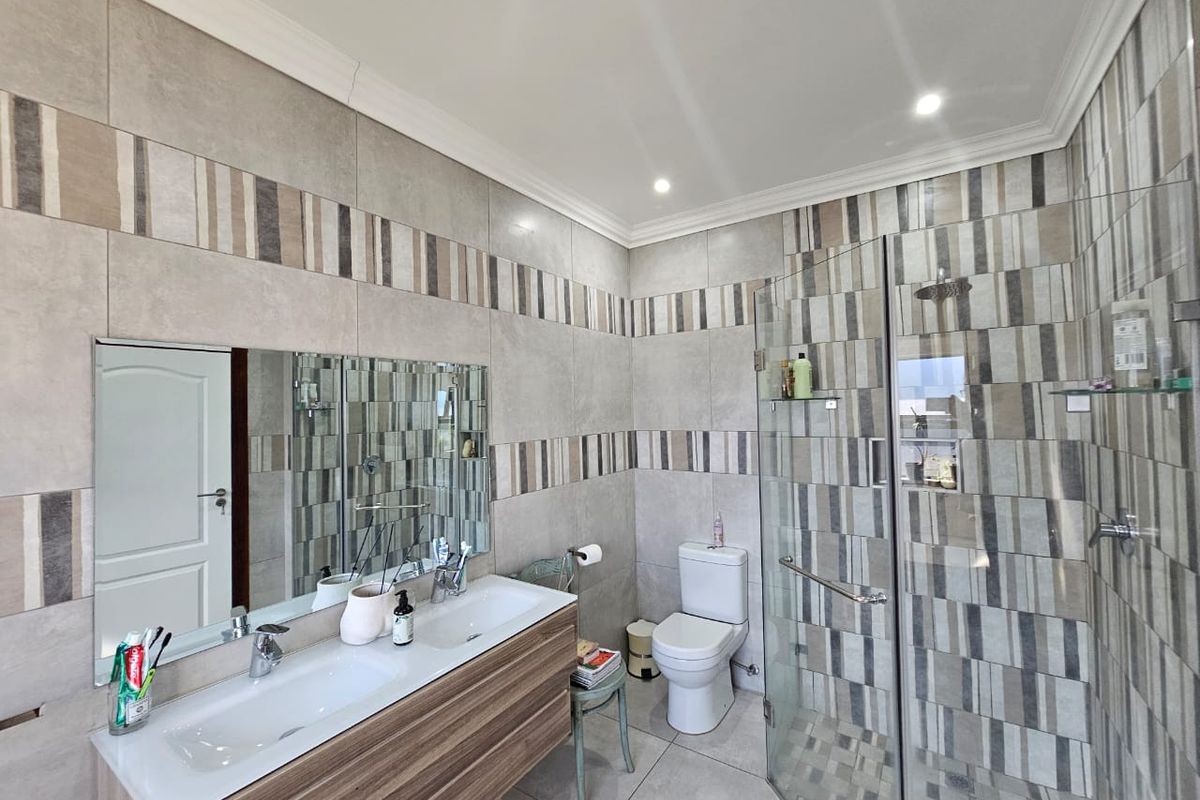 Modern bathroom featuring a double vanity, glass-enclosed shower, and contemporary patterned wall tiling with recessed lighting.