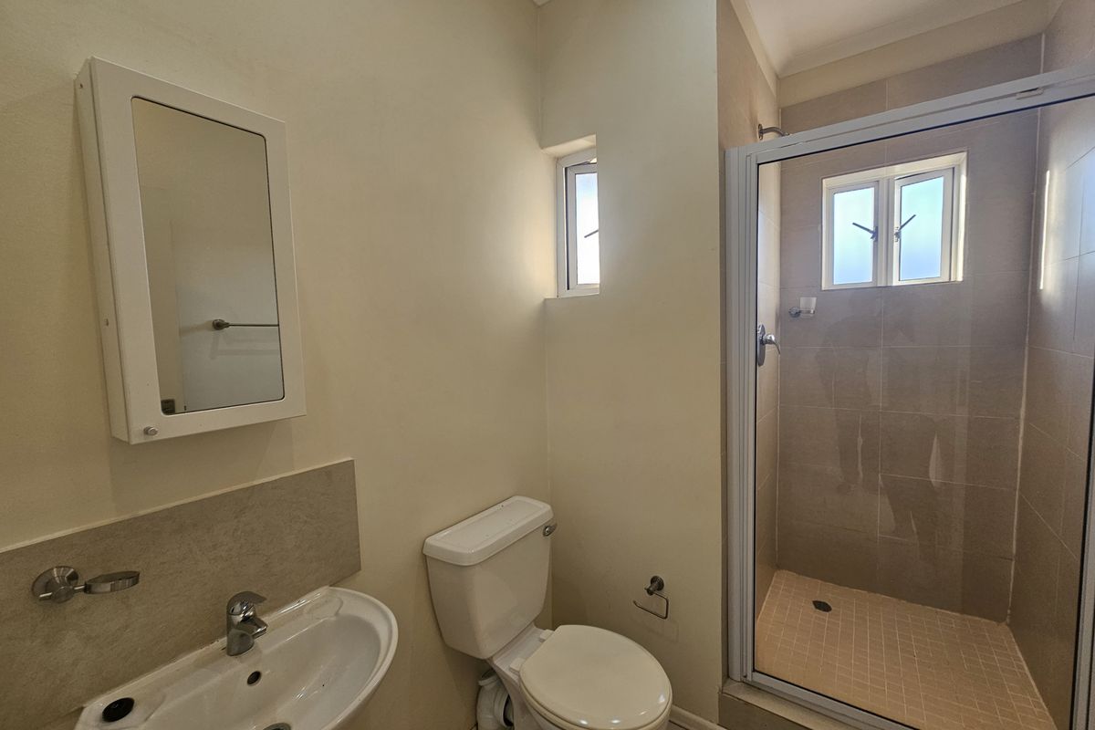 A functional bathroom featuring a pedestal basin, a toilet, and a glass-enclosed shower with tiled flooring.