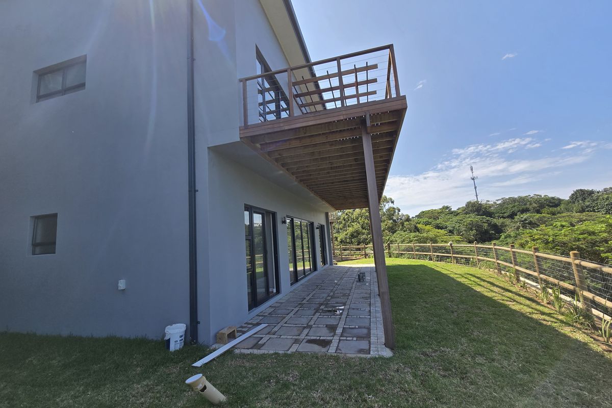Rear view of the property featuring a paved patio area and an elevated wooden balcony with a timber railing overlooking the garden.