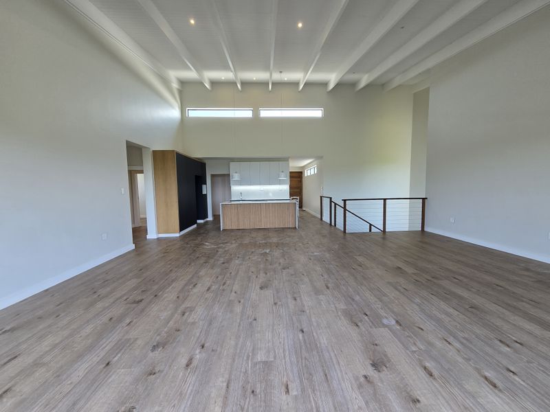 Spacious open-plan living area featuring high vaulted ceilings with exposed beams, modern kitchen island, and light wood-look flooring.