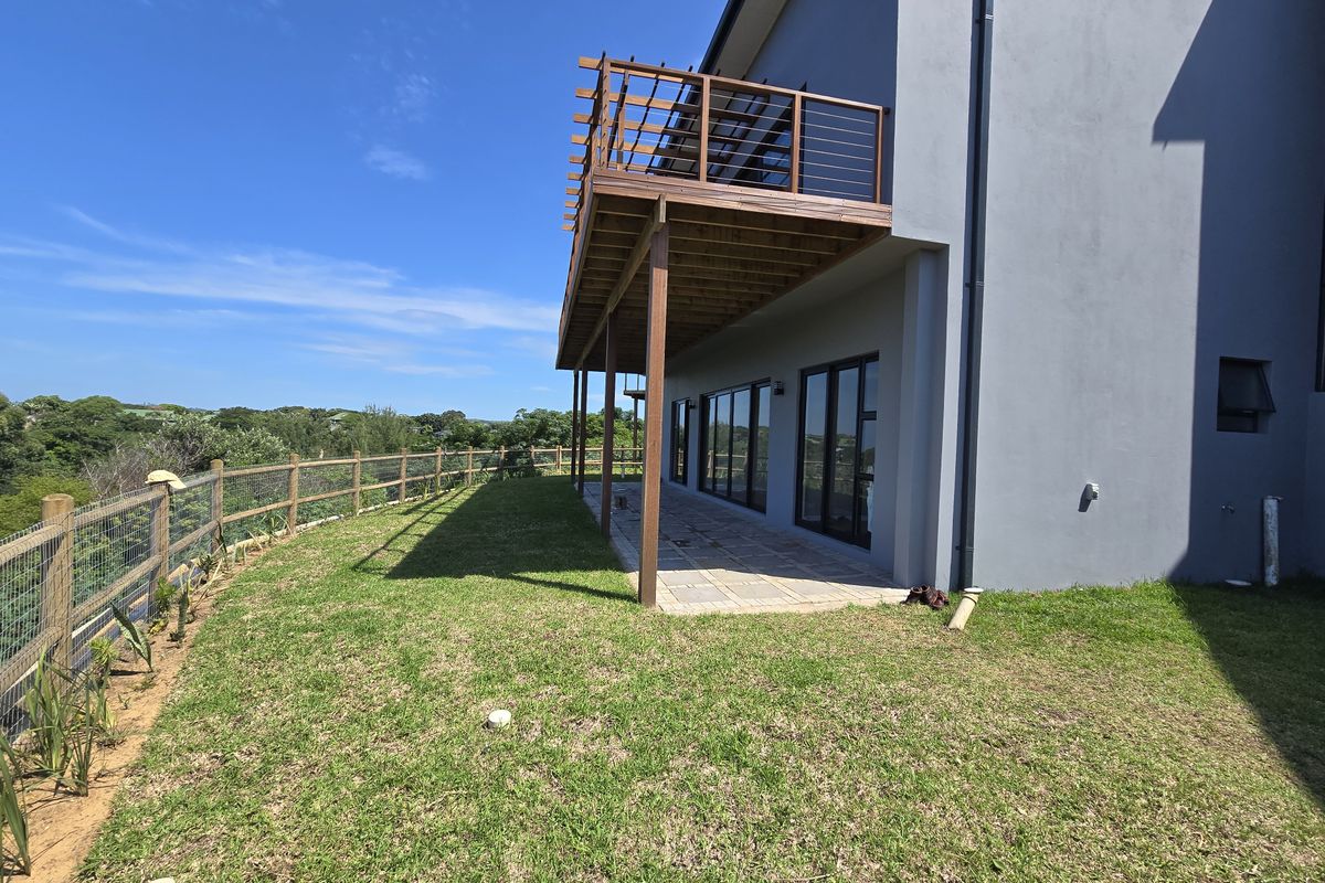 Rear view of the property featuring a paved patio area, a wooden balcony with railing, and a landscaped garden with perimeter fencing.
