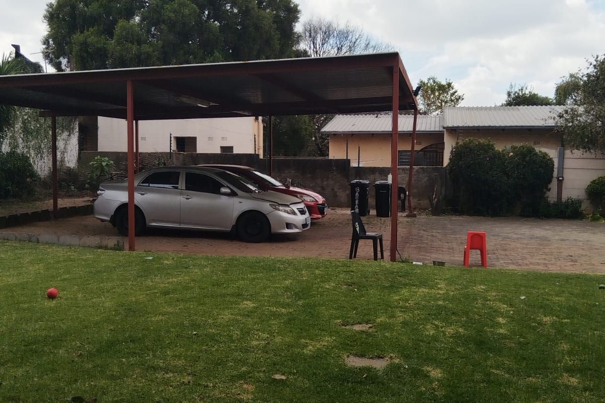 A spacious backyard featuring a large metal carport structure providing covered parking, set against a lawn area with perimeter boundary walls.