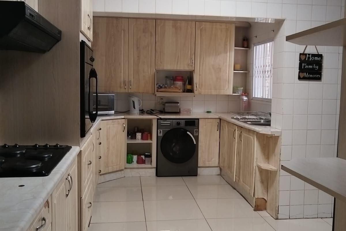 A functional kitchen featuring light wood cabinetry, tiled splashbacks, integrated oven, gas hob, extractor fan, and built-in laundry appliance space.
