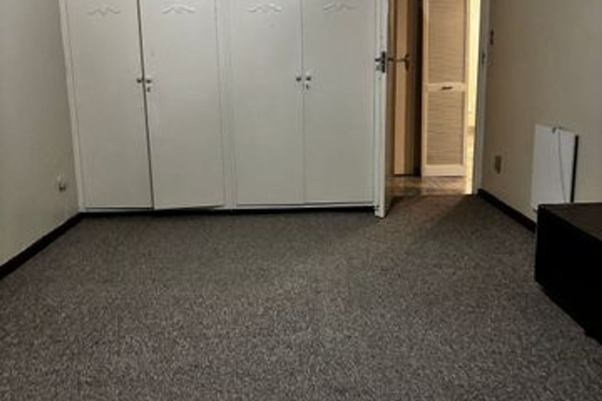 A bedroom featuring built-in floor-to-ceiling cabinetry and carpeted flooring, with an adjacent doorway leading to another area of the apartment.
