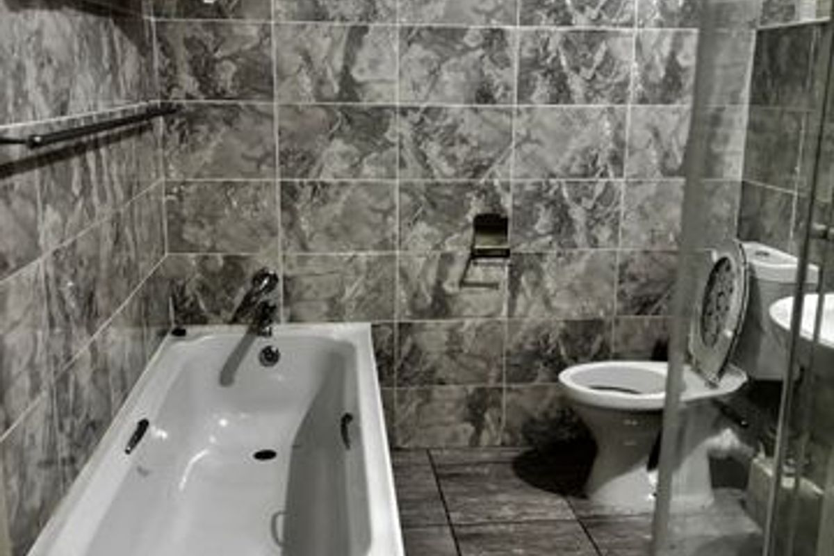 A compact bathroom featuring full-height marble-effect wall tiling, a built-in bathtub, a standard toilet, and a glass-enclosed shower unit.