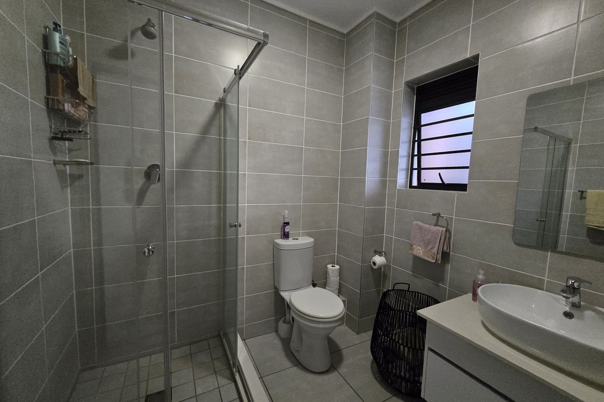 Modern bathroom featuring a glass-enclosed shower, wall-mounted vanity with a vessel sink, and neutral floor-to-ceiling tiling.