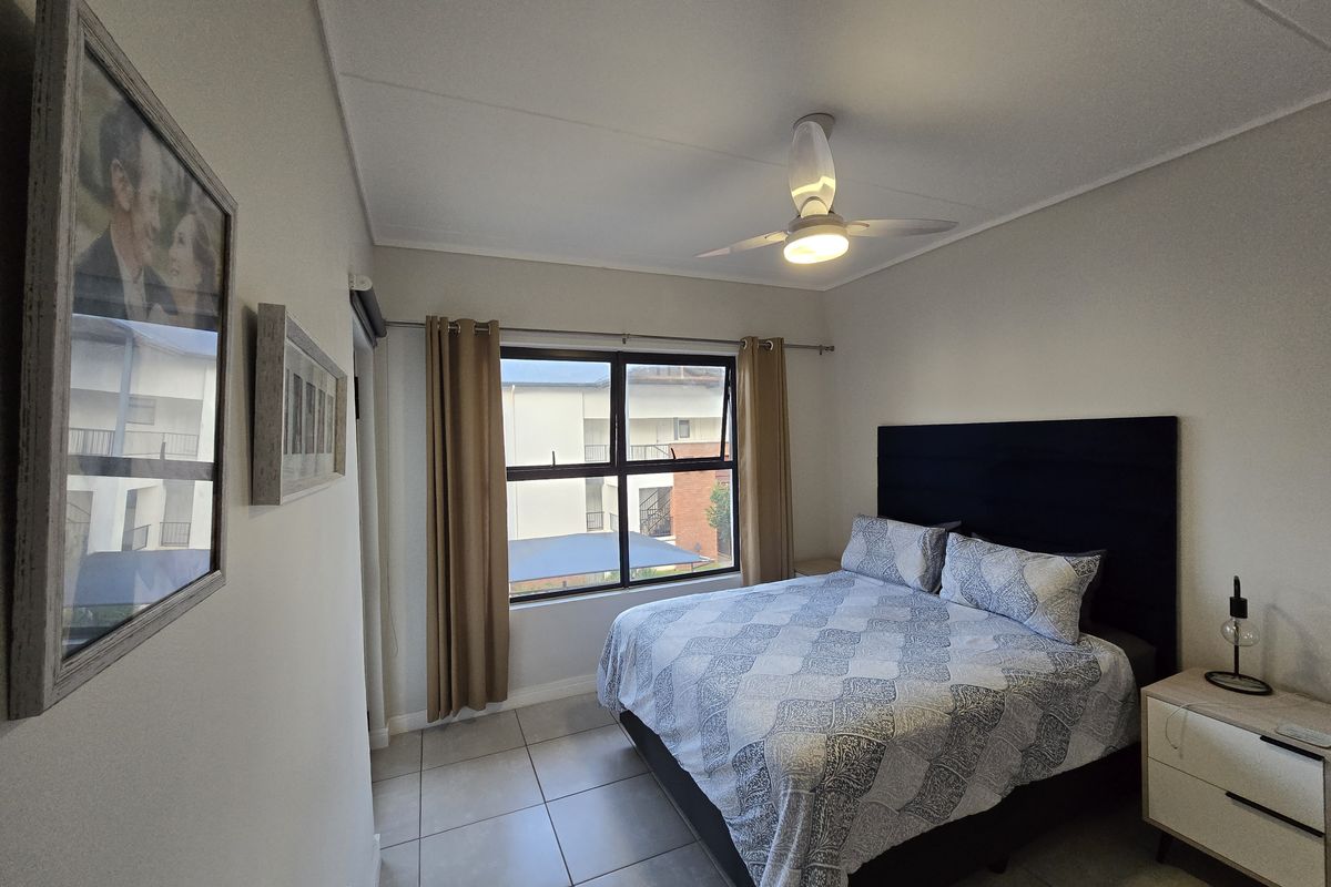 A well-maintained bedroom featuring tiled flooring, a ceiling fan, and a large window providing natural light.