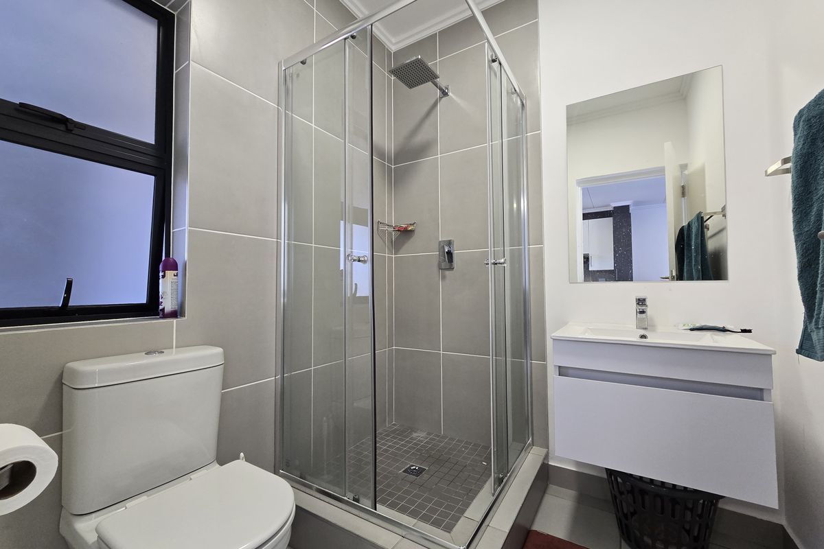 Modern bathroom featuring a glass-enclosed shower, wall-mounted vanity with basin, and a contemporary toilet, finished with neutral grey wall tiles.