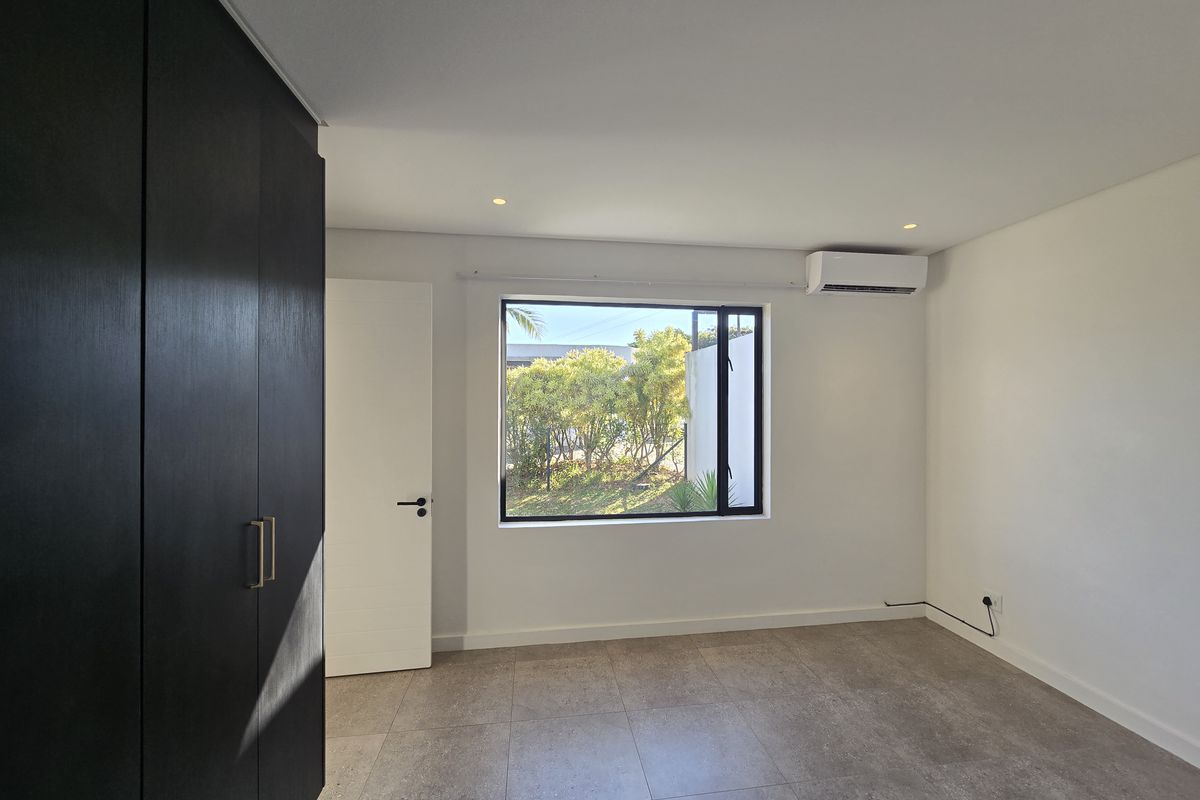 A bright, modern bedroom featuring neutral tiled flooring, built-in dark cabinetry, and a wall-mounted air conditioning unit.
