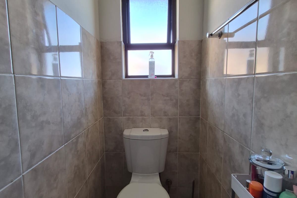 A compact bathroom featuring neutral ceramic wall and floor tiles, a standard toilet, and a top-hung window for natural ventilation.