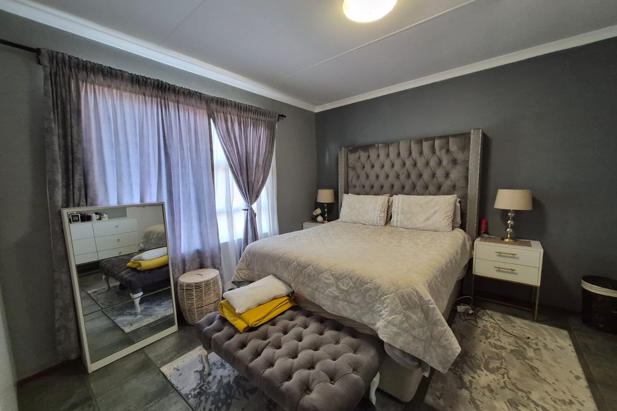 A well-maintained bedroom featuring dark grey walls, tiled flooring, and large windows with curtain treatments.