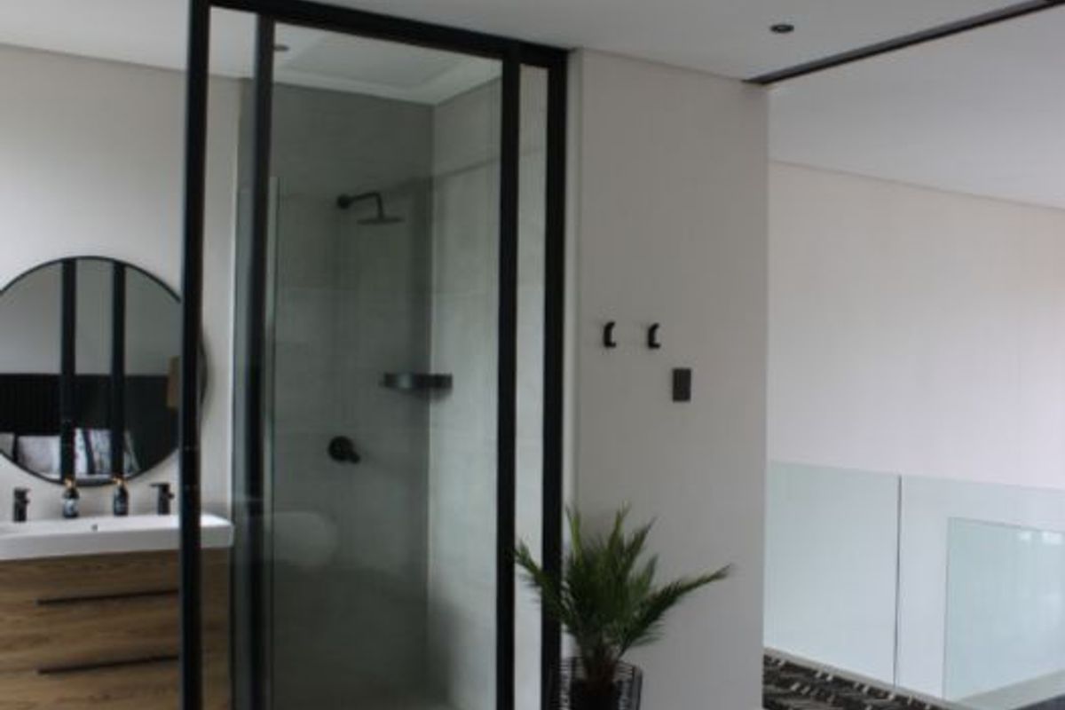 Modern bathroom featuring a sleek vanity, black-framed glass shower enclosure with rain shower head, and contemporary finishes.