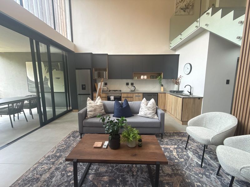 Modern open-plan living area featuring a sleek kitchen with built-in appliances, high ceilings, and large sliding doors leading to an outdoor patio space.