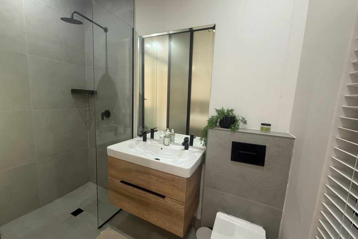 Modern bathroom featuring a walk-in shower with rain head, wall-hung timber vanity, black fixtures, and a concealed cistern toilet with grey tiling.