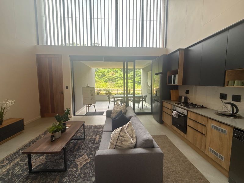 Modern open-plan living area featuring a sleek kitchen with built-in appliances, double volume ceilings, and seamless flow to a covered patio.