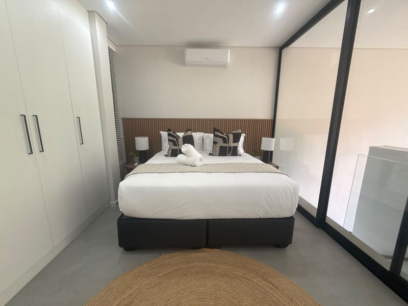 Modern bedroom featuring built-in cupboards, a stylish slatted timber headboard, wall-mounted air conditioning, and a contemporary glass partition wall.