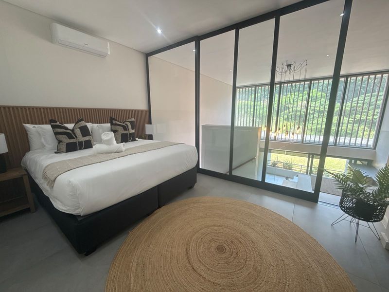 Modern bedroom featuring a timber slat headboard, split-system air conditioning, and a sleek black-framed glass partition overlooking the lower level.