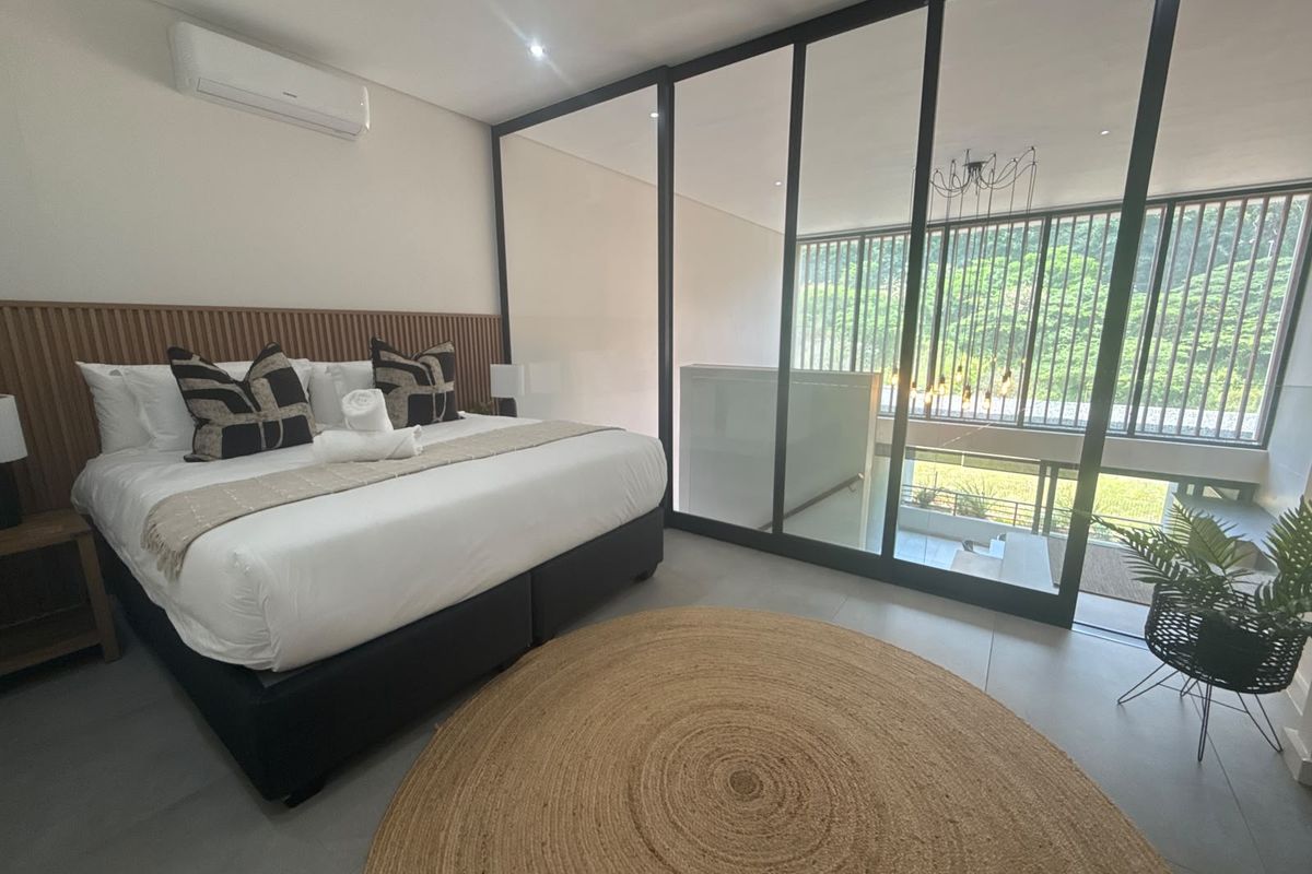 Modern bedroom featuring a timber slat headboard, split-system air conditioning, and a sleek black-framed glass partition overlooking the lower level.