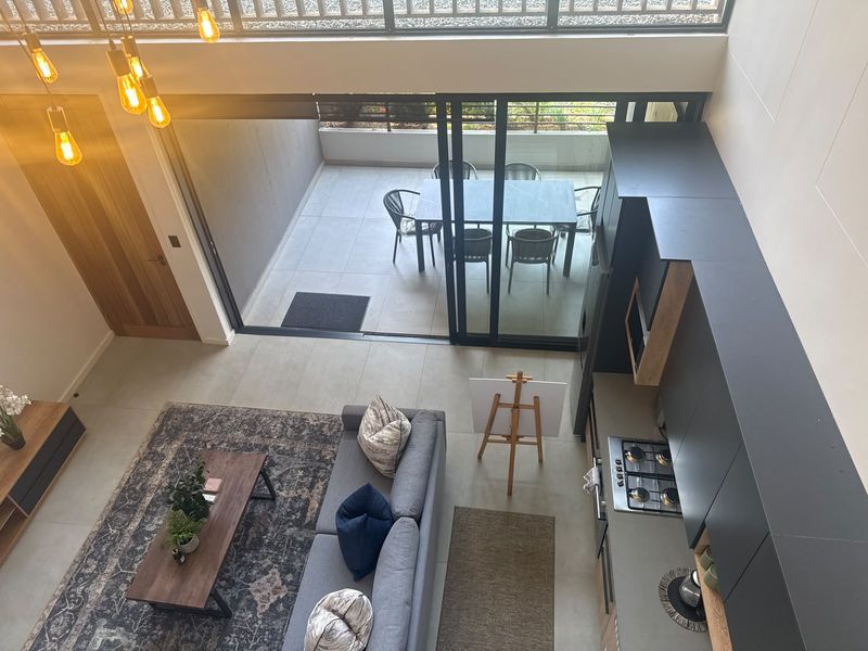 Modern open-plan living area featuring a sleek kitchen with built-in appliances, tiled floors, and seamless flow to a private balcony through large sliding doors.