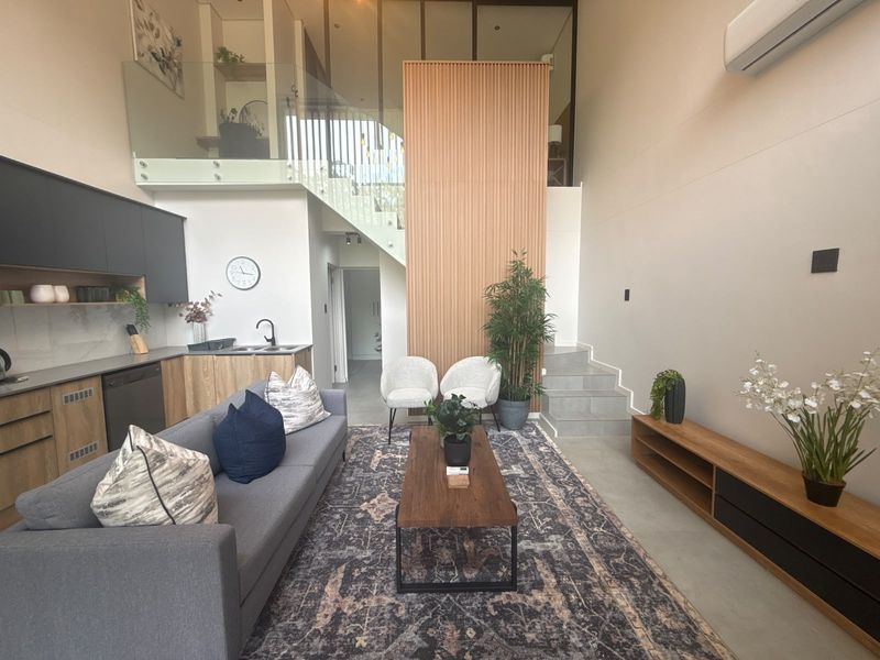 Modern open-plan living area featuring a sleek kitchen, double-volume ceilings, a striking timber slat feature wall, and a contemporary staircase with glass balustrades.