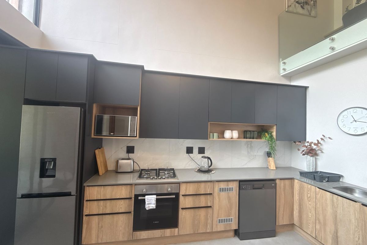 Modern kitchen featuring matte charcoal and wood-grain cabinetry, stone countertops, integrated appliances, and a high-ceiling design with a glass mezzanine balustrade.