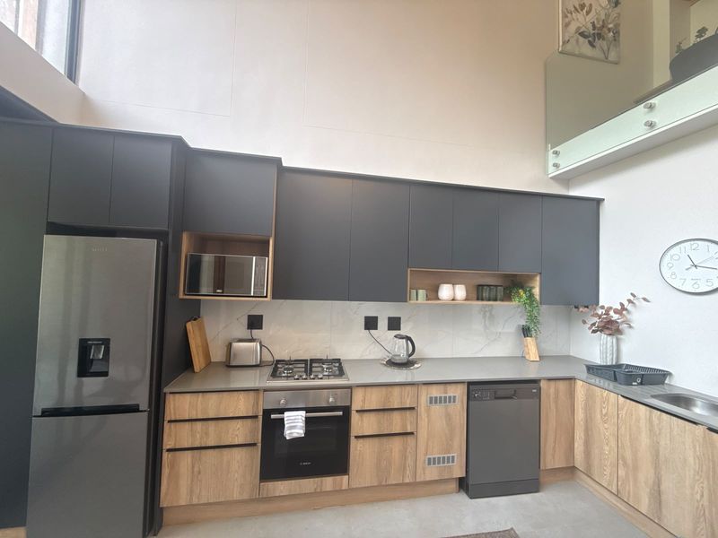 Modern kitchen featuring matte charcoal and wood-grain cabinetry, stone countertops, integrated appliances, and a high-ceiling design with a glass mezzanine balustrade.
