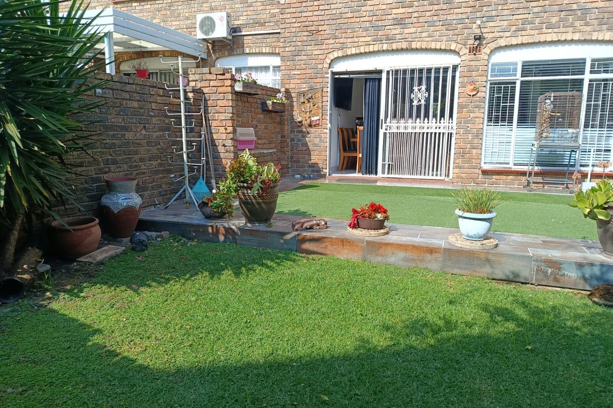 A private rear garden featuring a brick-paved facade, a raised tiled patio area, and a well-maintained lawn with integrated security gates.