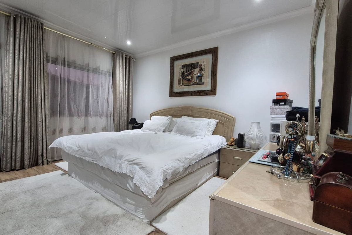 A well-lit bedroom featuring a glossy ceiling finish, neutral wall tones, and large window treatments, providing a comfortable and functional sleeping space.