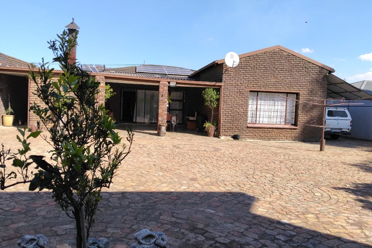 A rear exterior view of a brick house featuring a covered patio area, solar panels on the roof, and a paved courtyard.