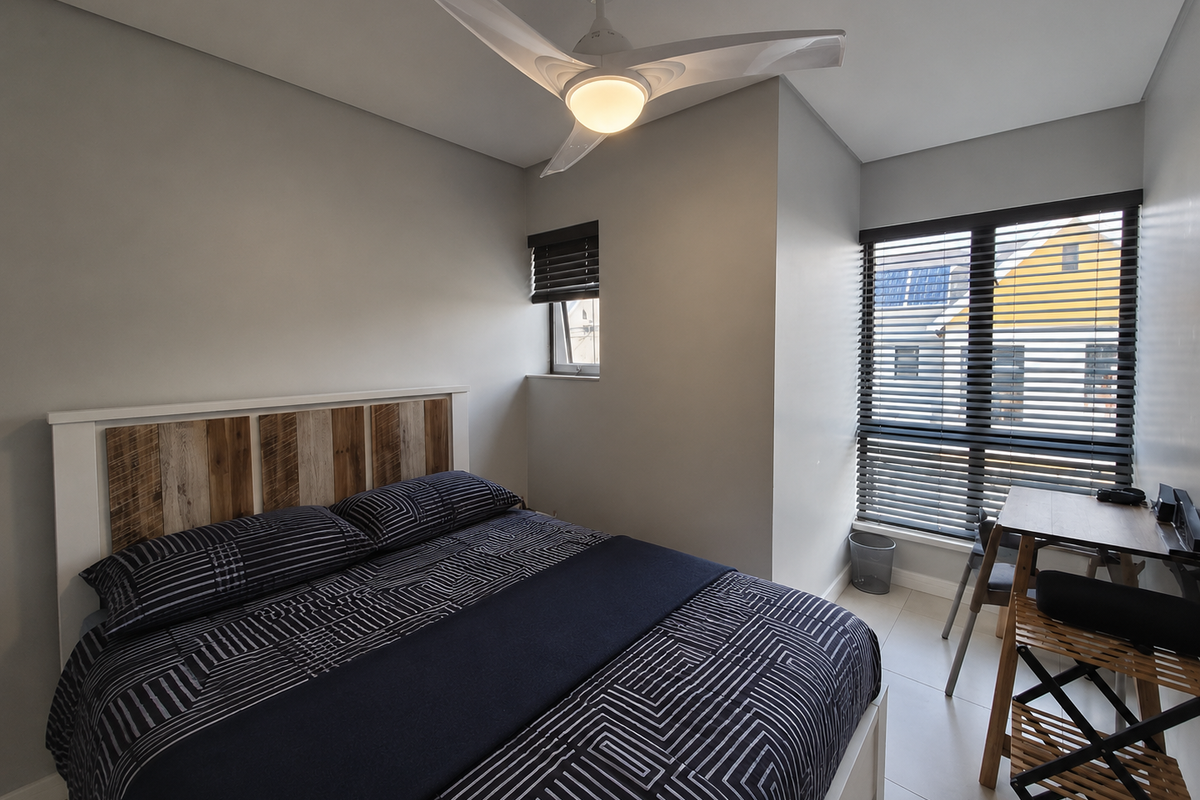 A modern bedroom featuring tiled flooring, a ceiling fan with integrated lighting, and large windows fitted with dark venetian blinds.