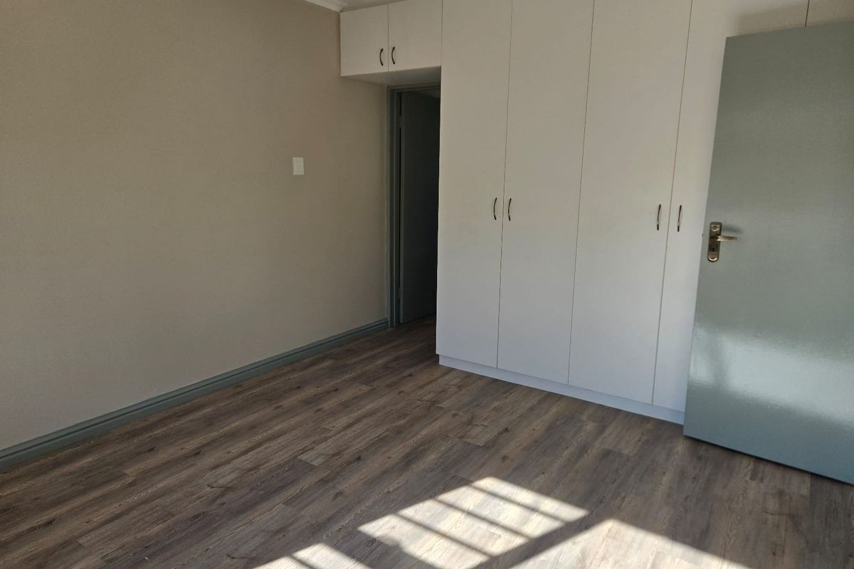 A bright, empty bedroom featuring modern wood-look laminate flooring and built-in white cabinetry with overhead storage.